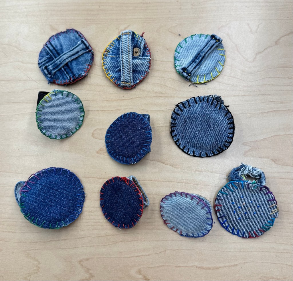 A collection of circular fabric patches made from denim, featuring various stitching styles and colors, arranged on a wooden surface.