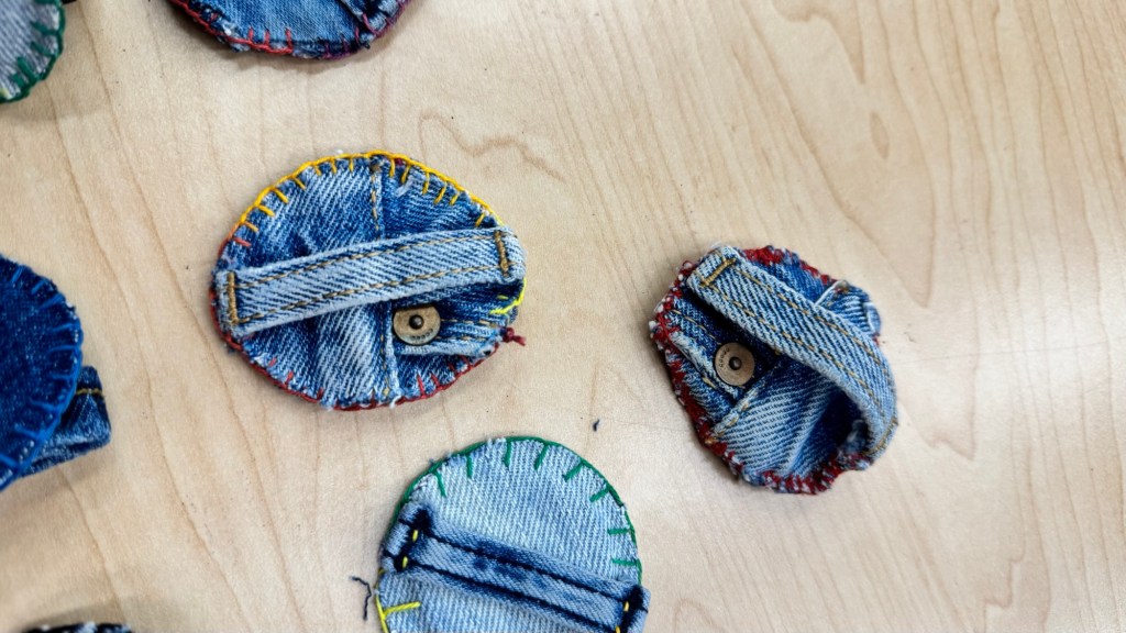 Several small round denim patches with colorful stitching, placed on a wooden surface.